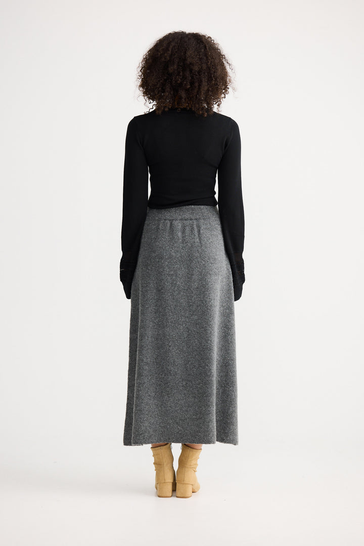 Person wearing a black top and gray skirt on a white background