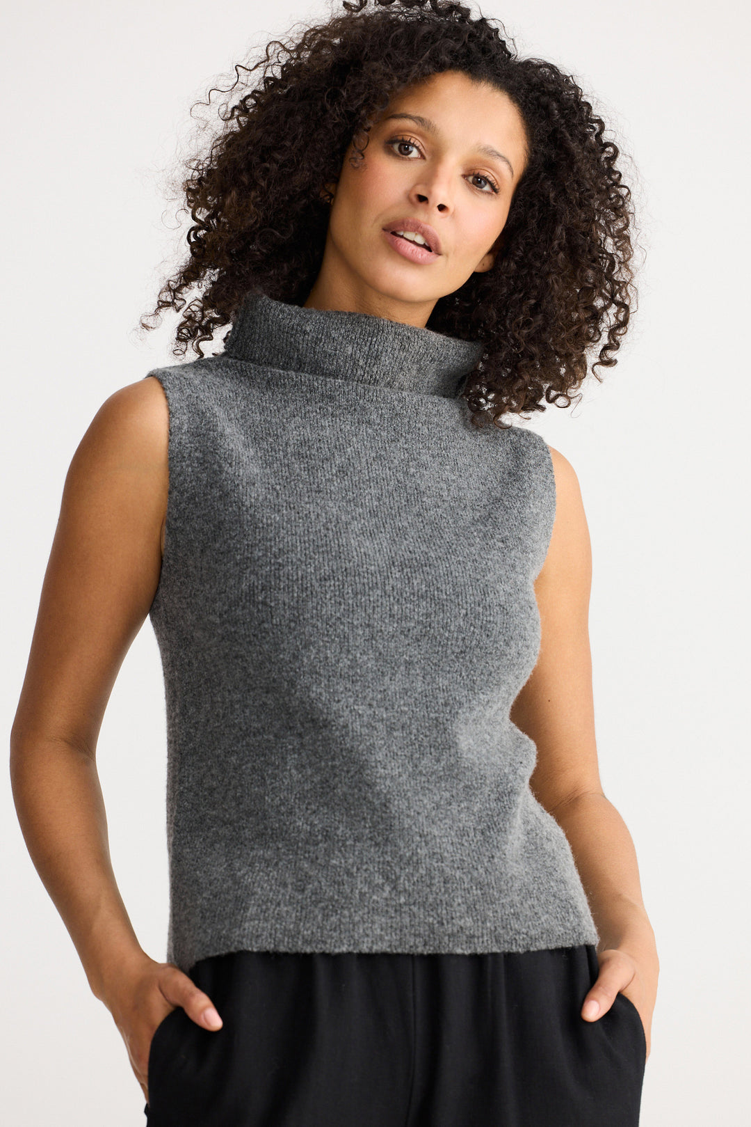 Woman wearing a gray sleeveless sweater against a white background