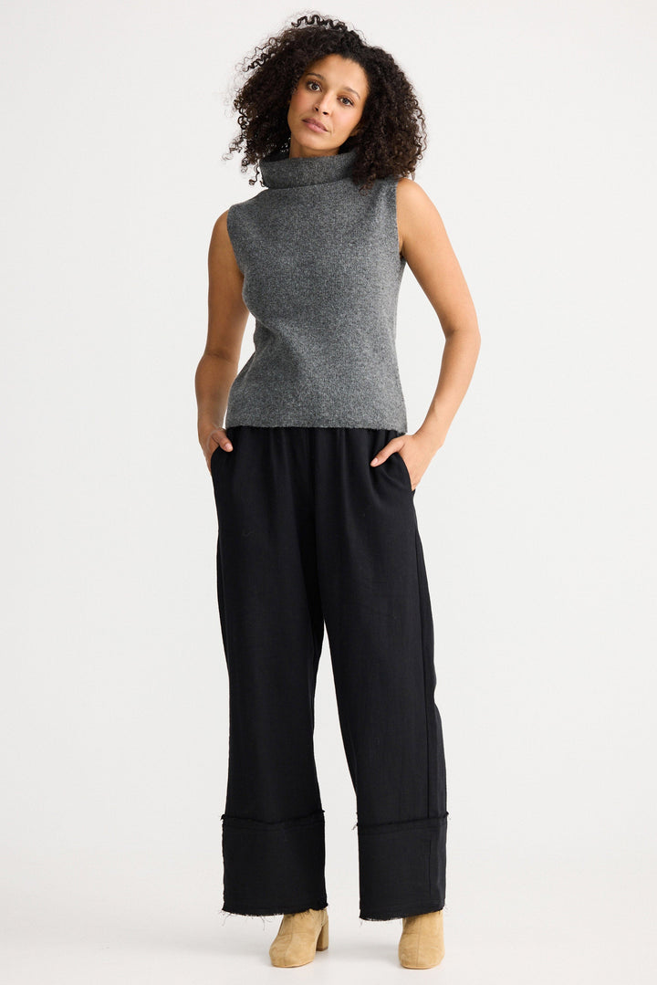 Woman wearing a sleeveless gray top and black pants on a white background