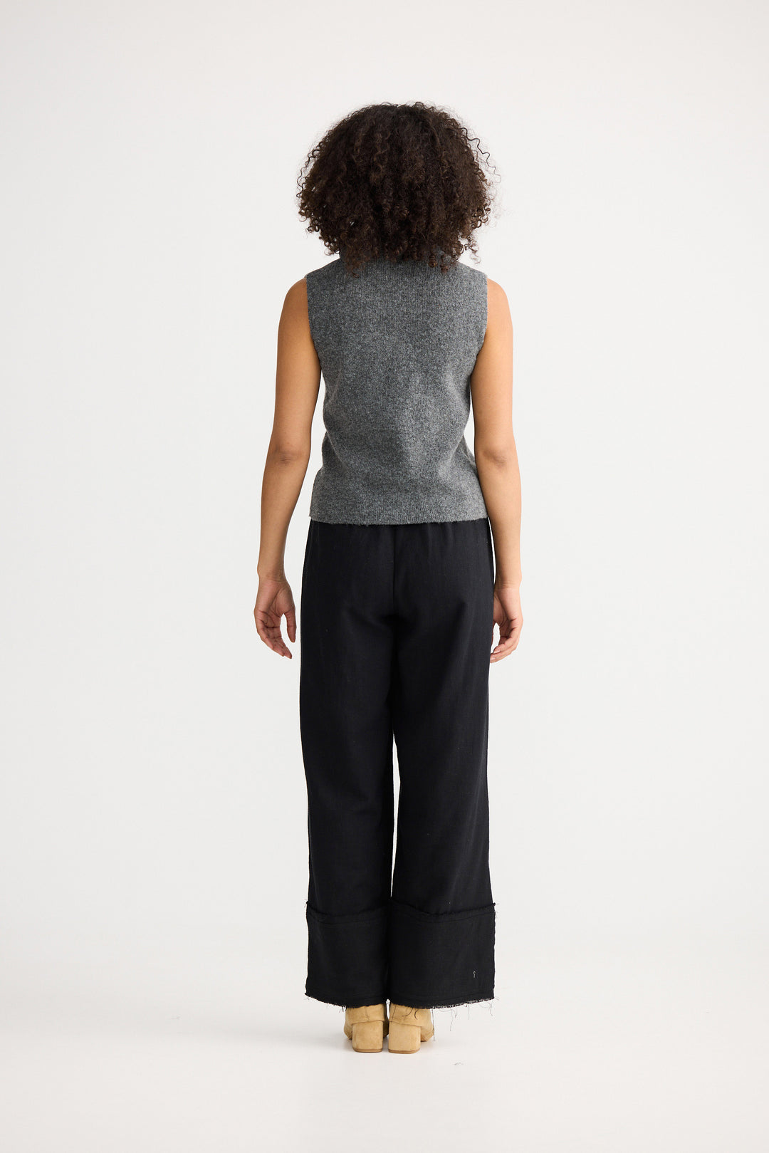 Person wearing a gray sleeveless top and black pants on a white background