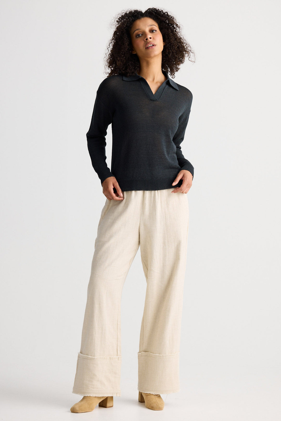 Woman wearing a dark sweater and light pants on a white background