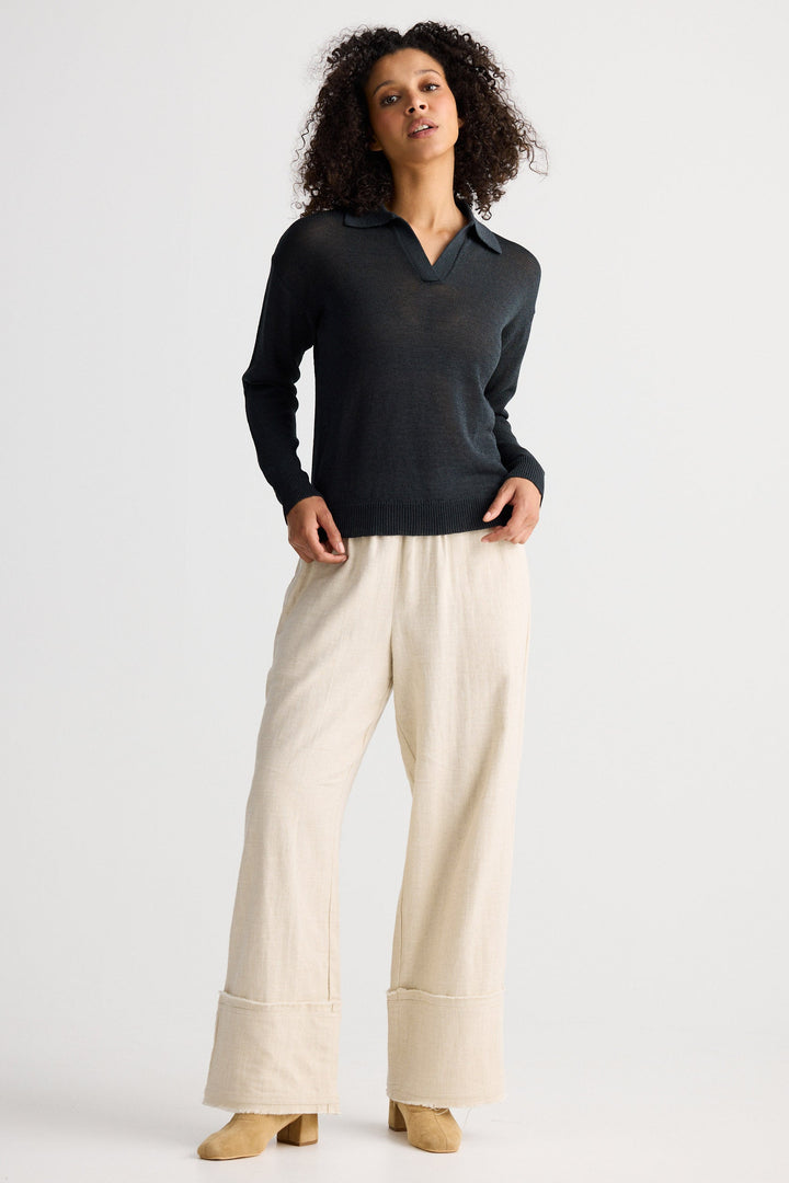 Woman wearing a dark sweater and light pants on a white background