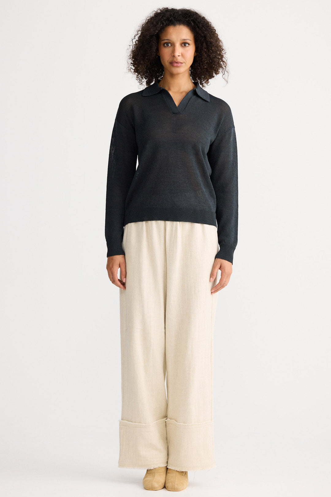 Woman wearing a dark gray sweater and beige pants on a white background