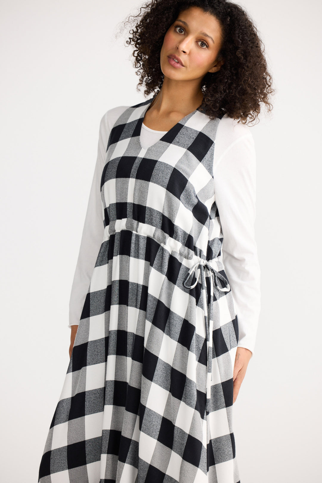 Woman wearing a black and white checkered dress with a white cardigan on a white background
