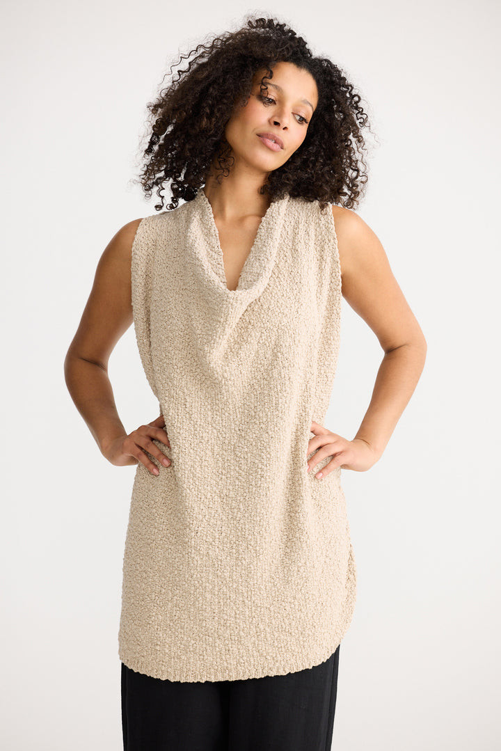 Woman wearing a beige sleeveless top against a white background