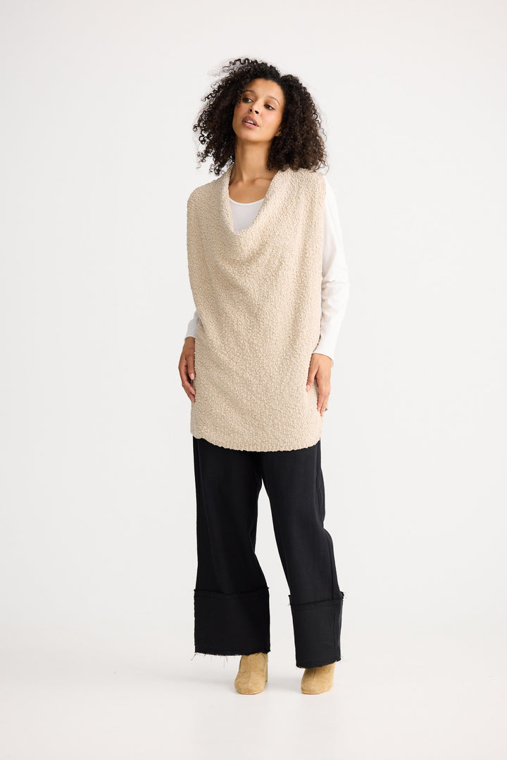 Woman wearing a beige knitted vest over a white shirt on a white background