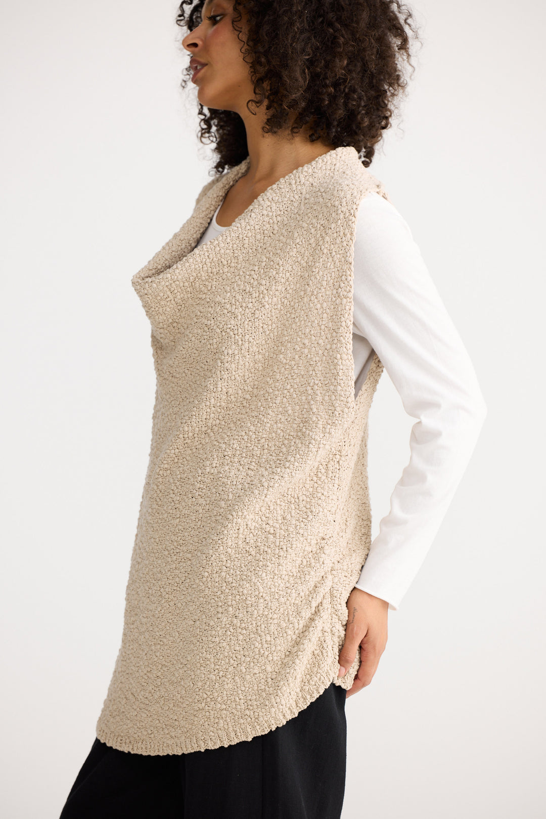 Woman wearing a beige knitted vest over a white shirt on a white background