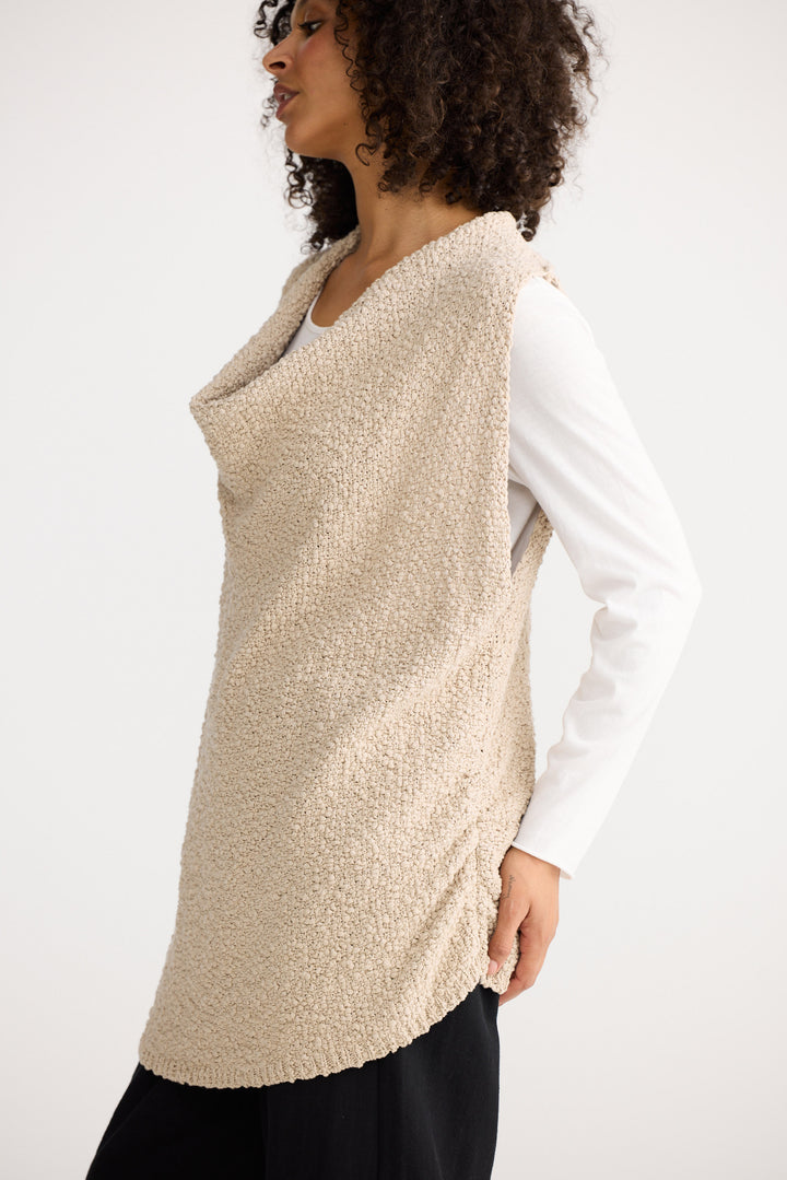 Woman wearing a beige knitted vest over a white shirt on a white background