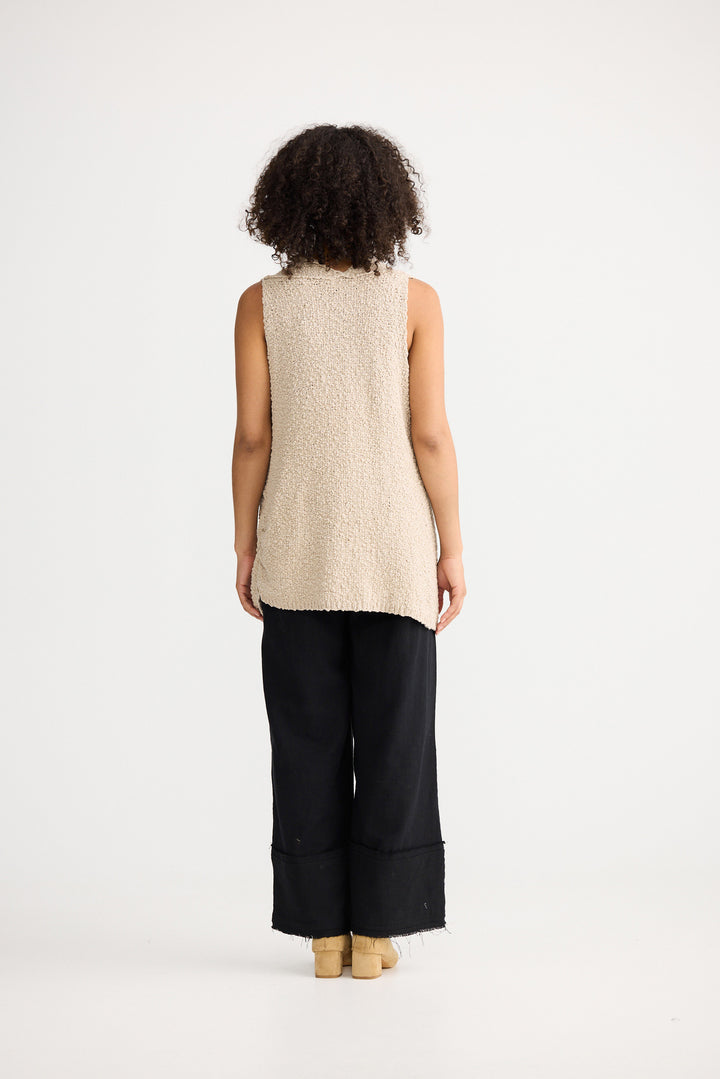 Person wearing a beige sleeveless top and black wide-leg pants on a white background