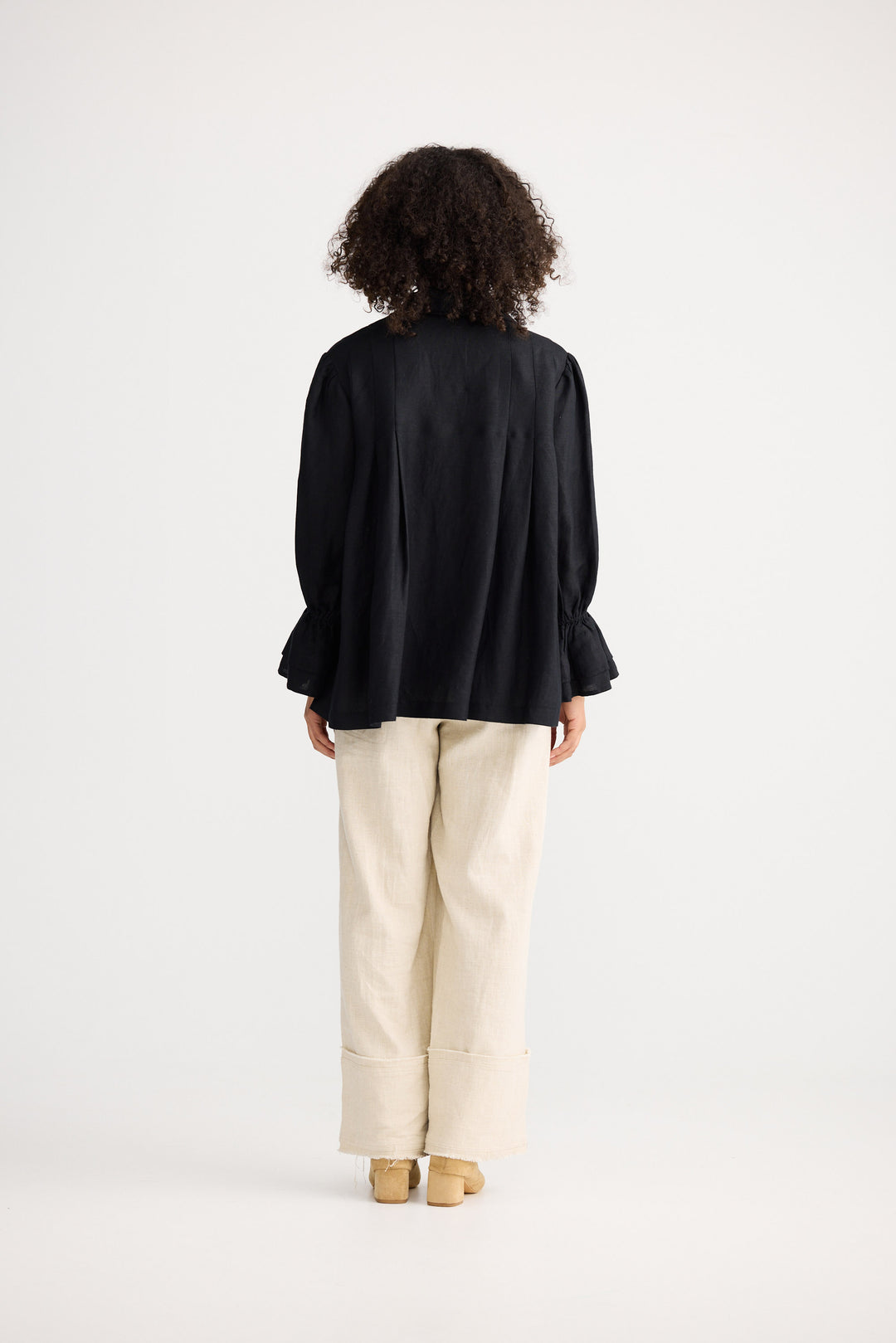 Person wearing a black top and beige pants standing against a white background