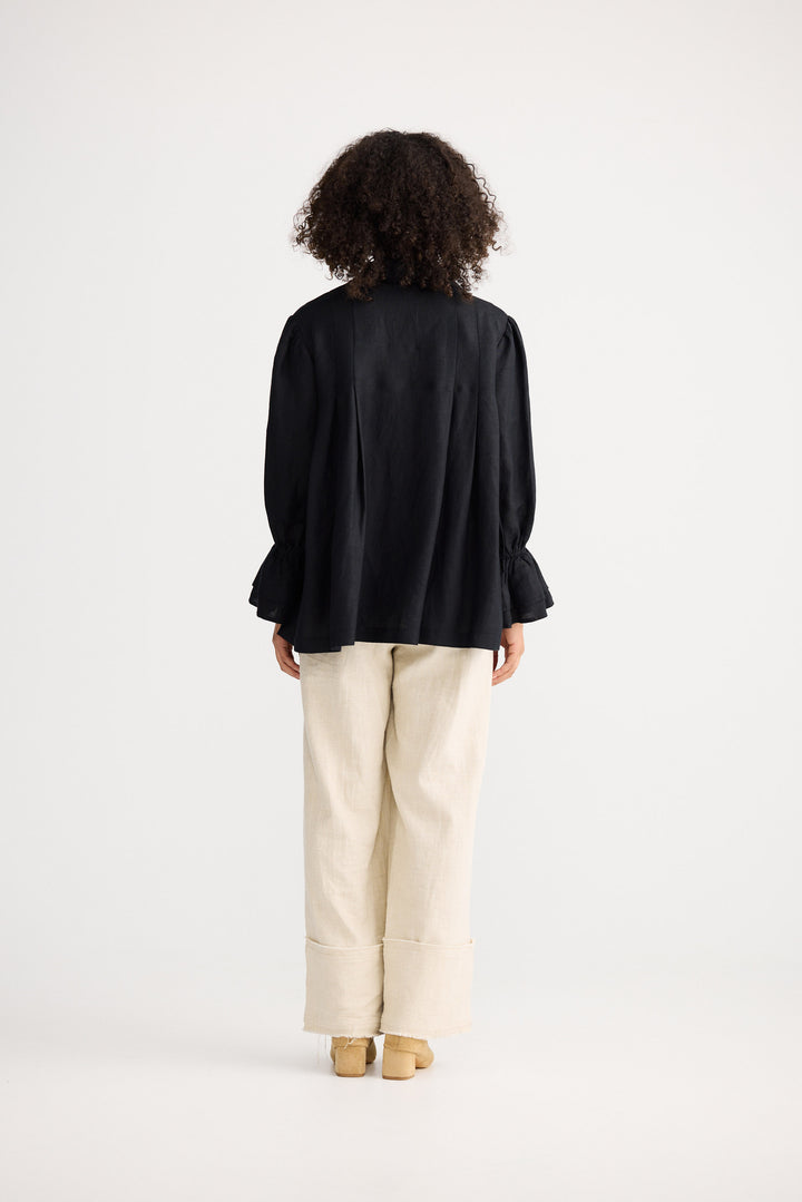 Person wearing a black top and beige pants standing against a white background