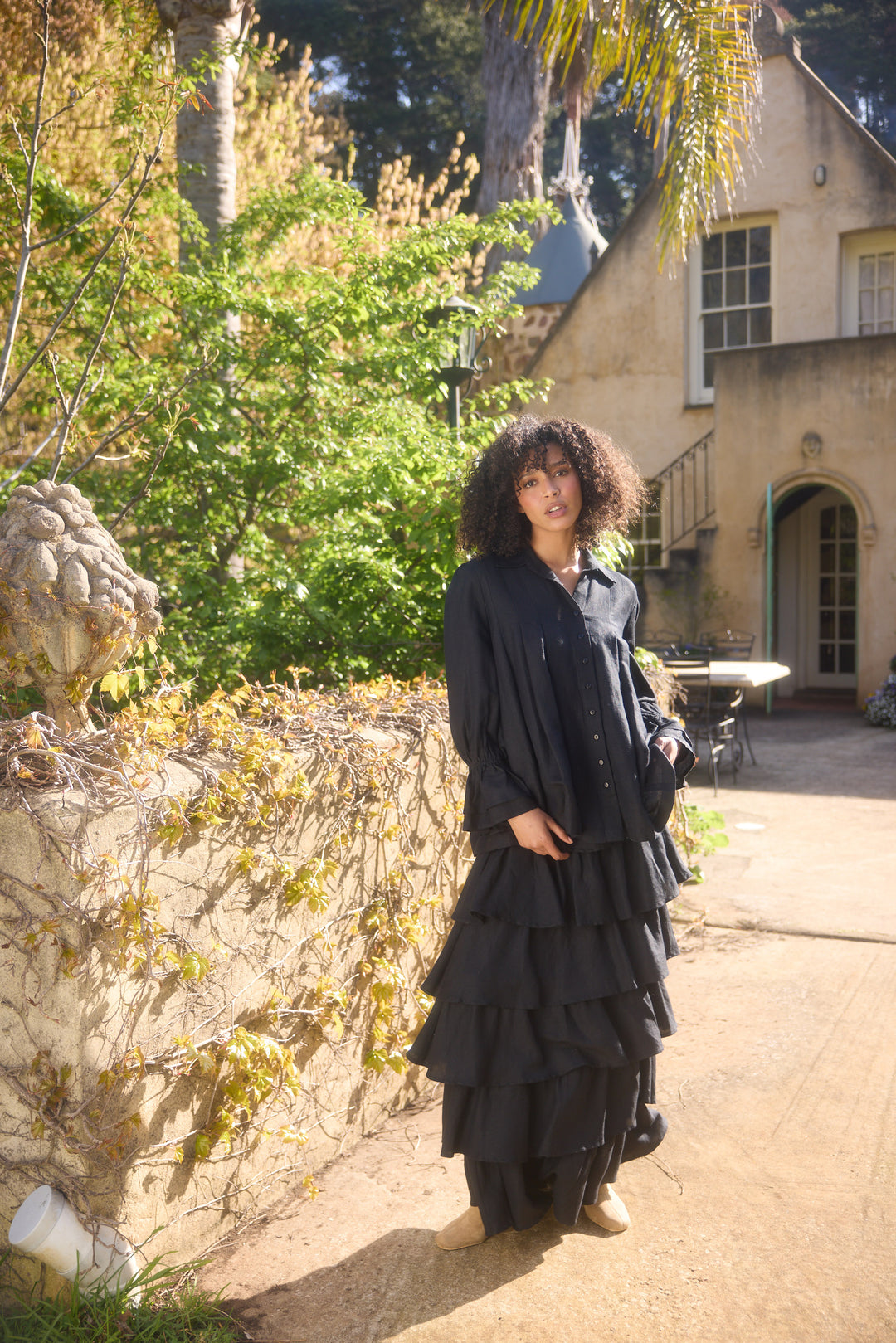Woman in a black dress standing outdoors near a stone wall and building.