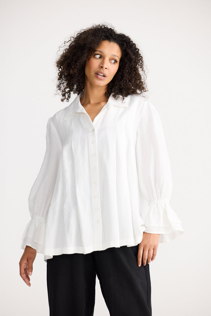 Woman wearing a white blouse and black pants against a white background