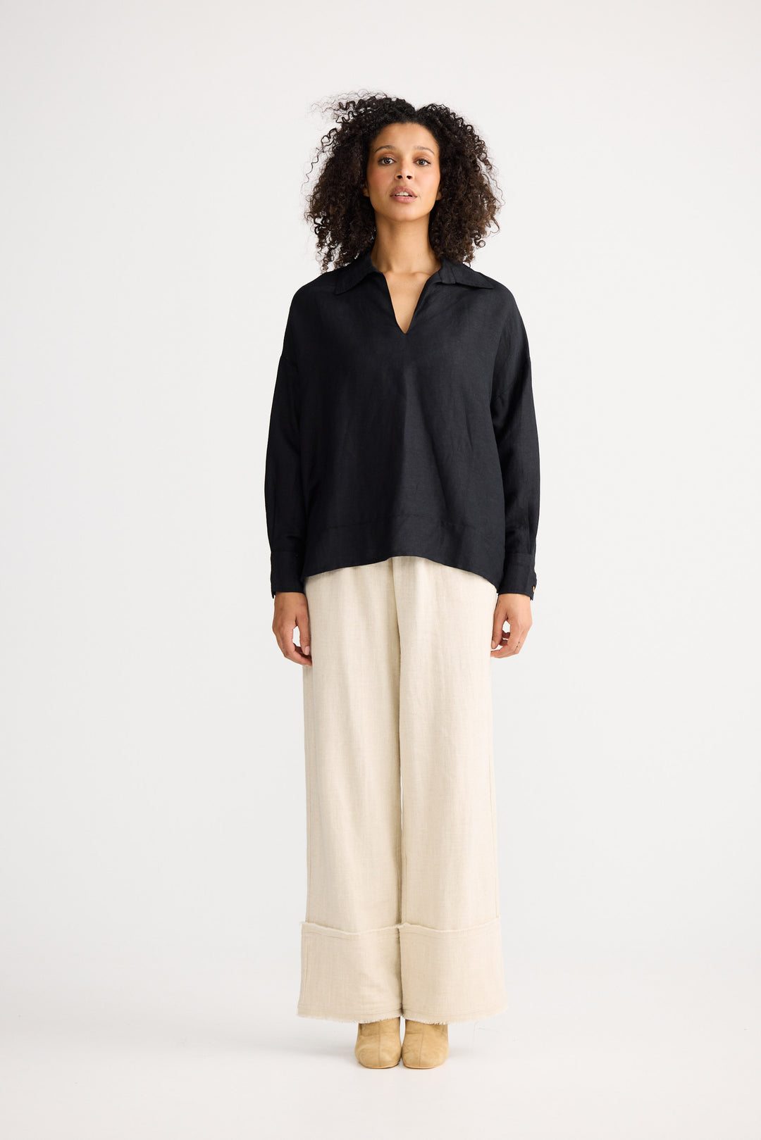 Woman wearing a black blouse and beige pants on a white background