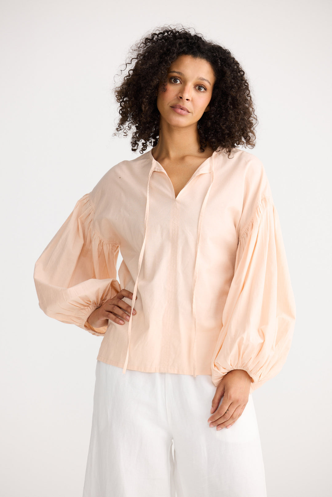 Woman wearing a light pink blouse and white pants on a white background