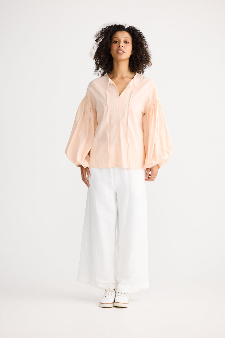 Woman wearing a light pink blouse and white pants on a white background
