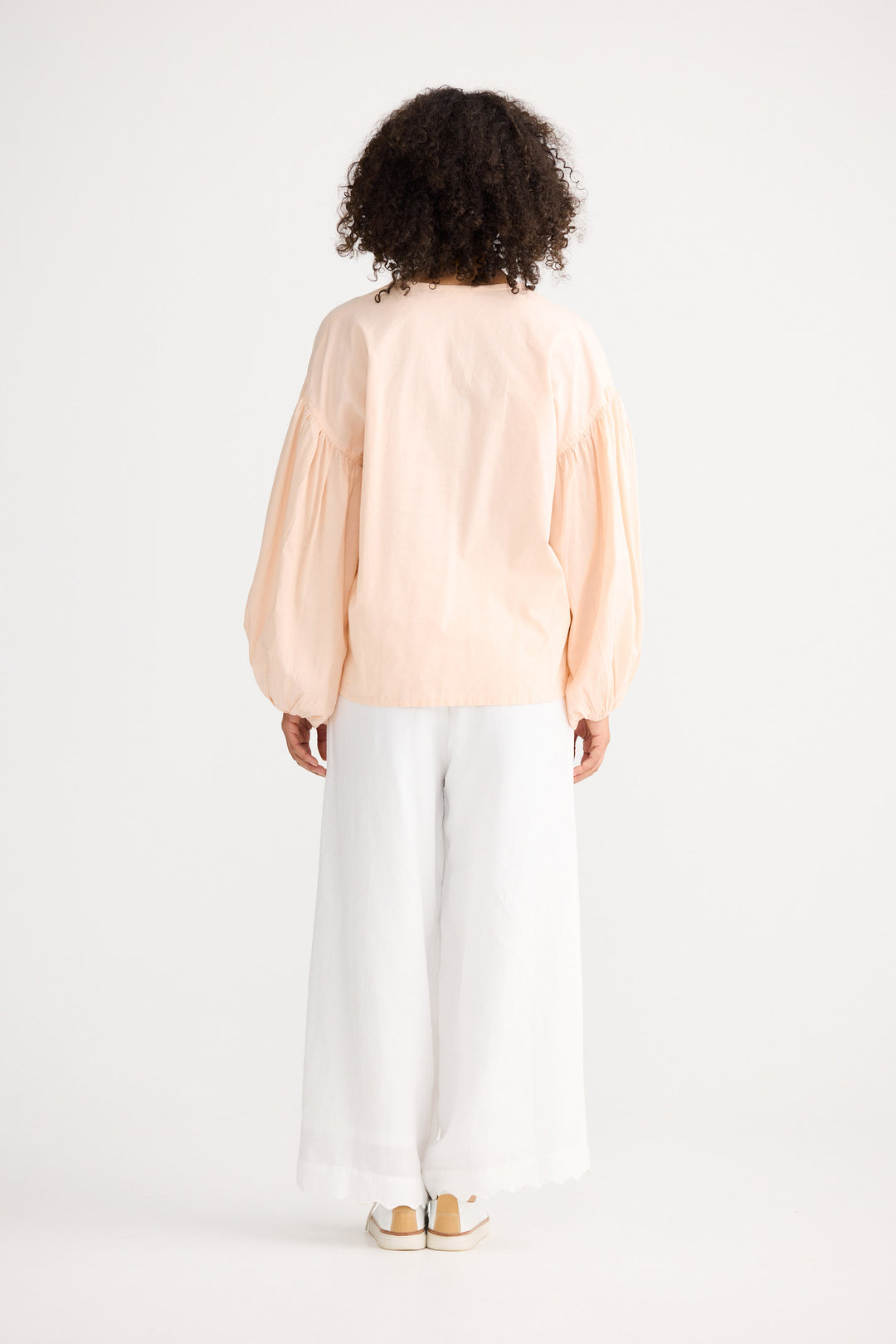 Person wearing a light pink blouse and white pants on a plain background