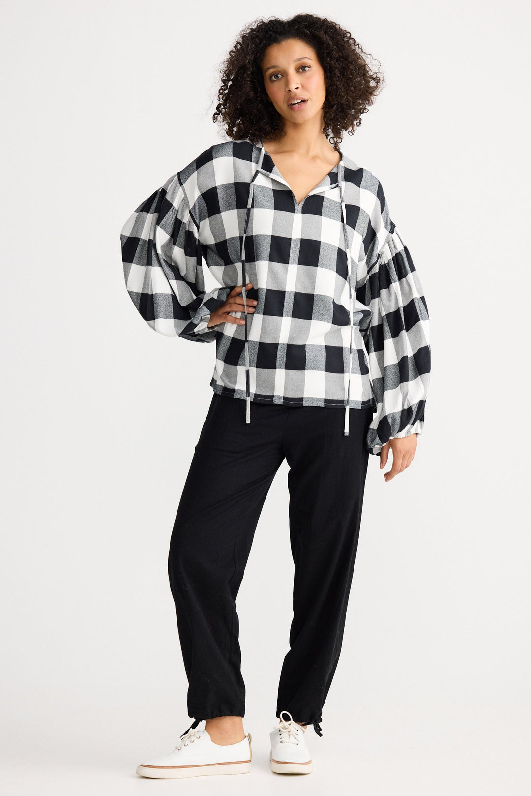 Woman wearing a black and white checkered shirt and black pants on a white background