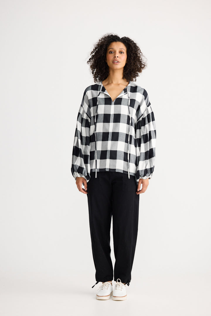 Woman wearing a black and white checkered shirt and black pants on a white background