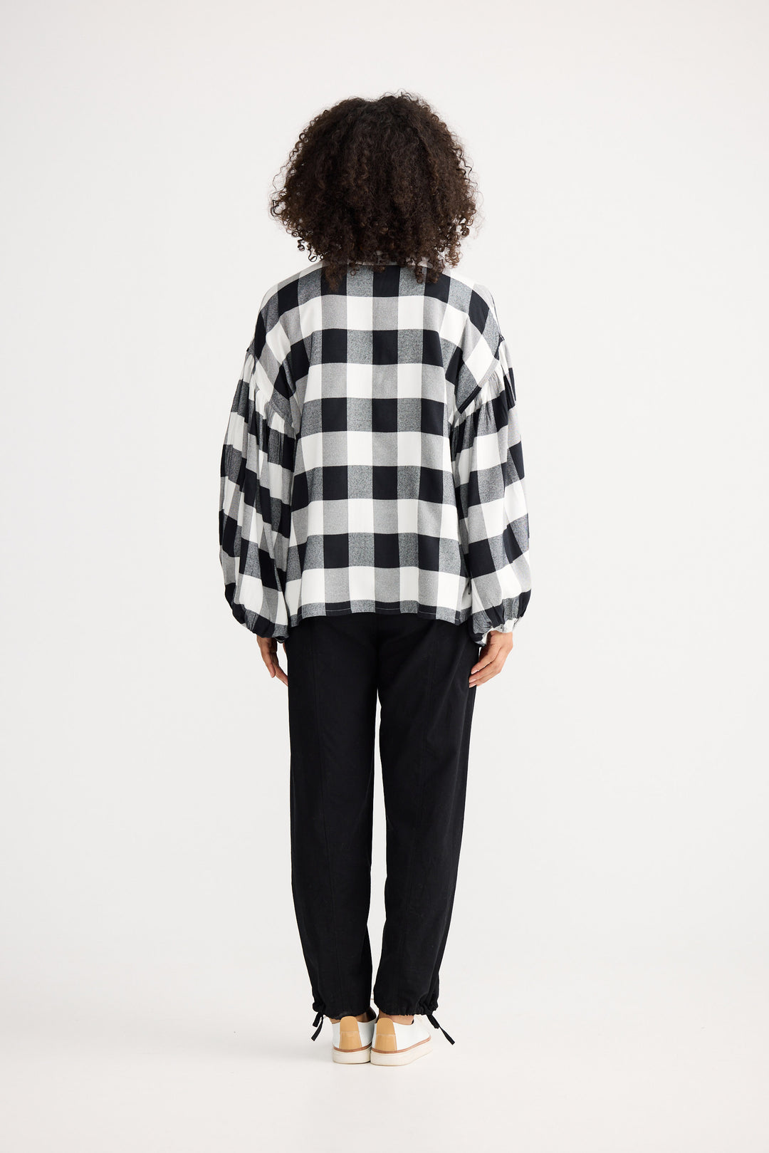 Person wearing a black and white checkered shirt and black pants on a white background