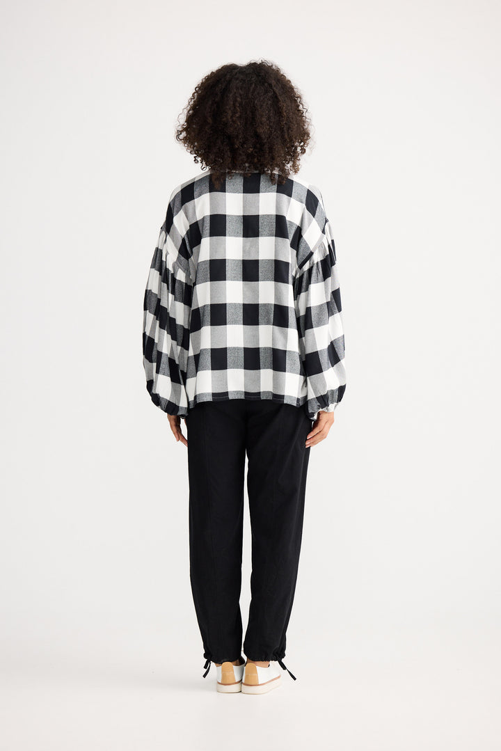 Person wearing a black and white checkered shirt and black pants on a white background