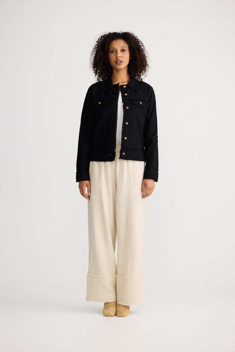 Woman wearing a black jacket and beige pants on a white background