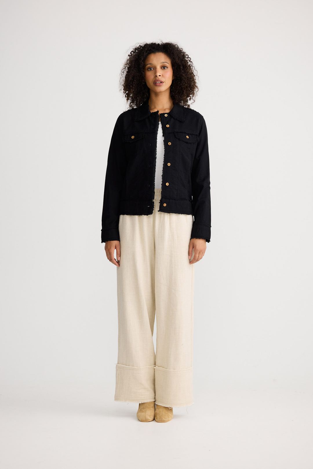 Woman wearing a black jacket and beige pants on a white background