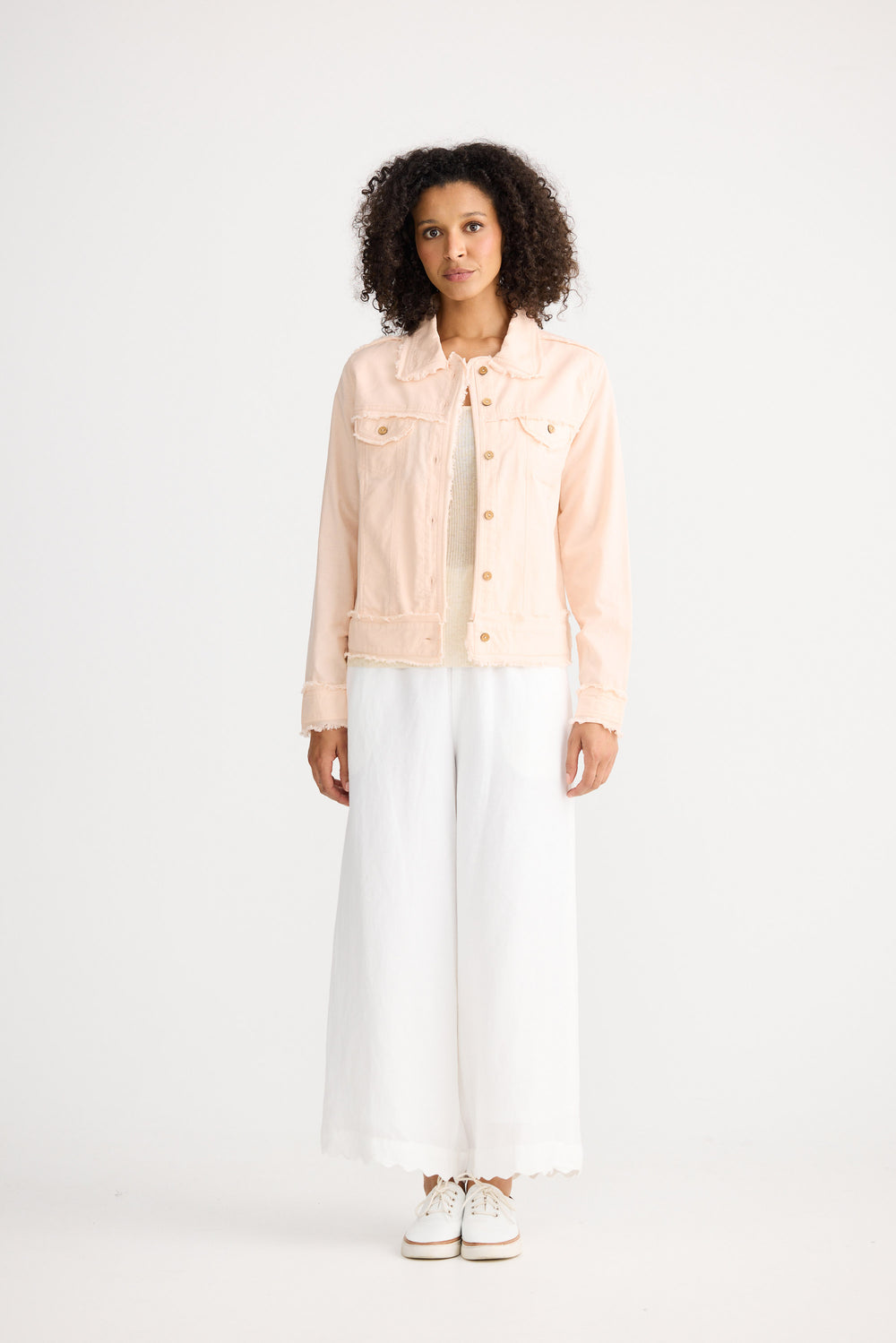 Woman wearing a light pink denim jacket over a white shirt and pants on a white background