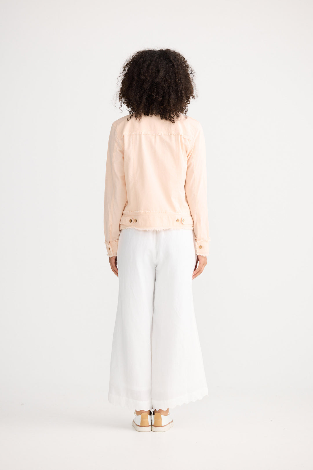 Person wearing a light pink blouse and white pants on a white background