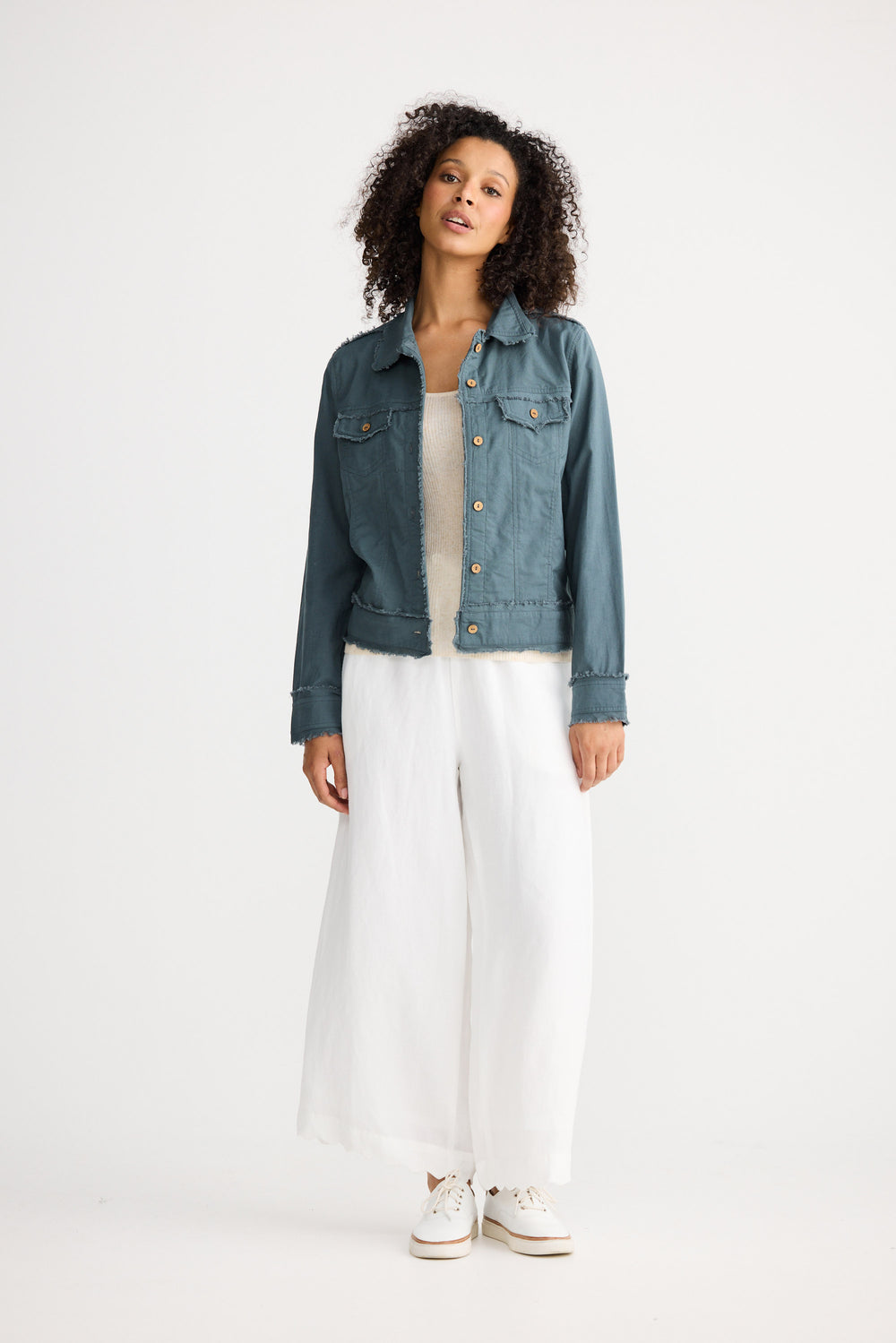 Woman wearing a denim jacket, white top, and white pants on a white background