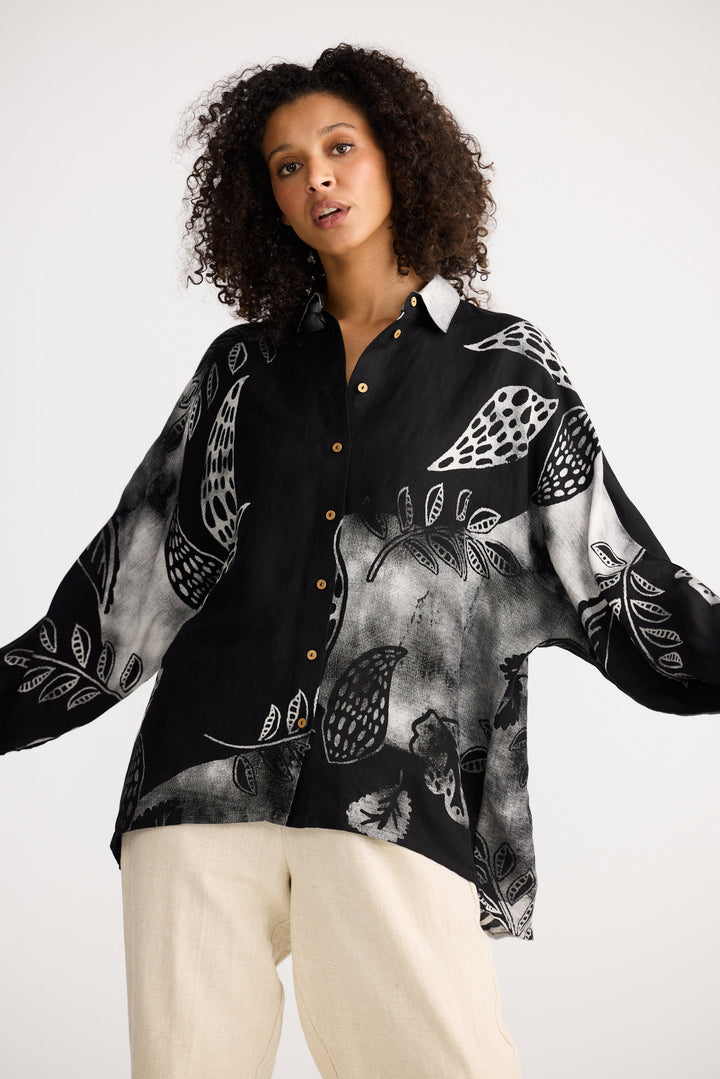 Woman wearing a black patterned blouse with beige pants on a white background