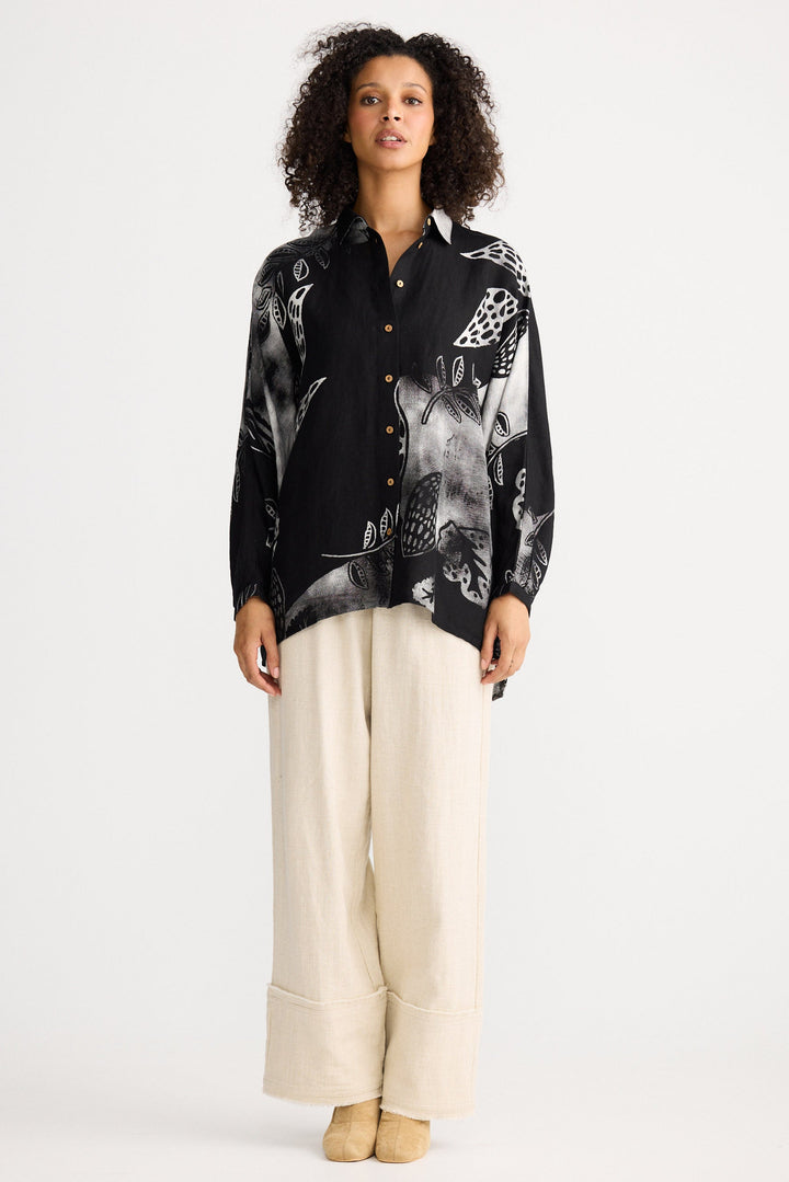 Person wearing a black patterned shirt and beige pants on a white background