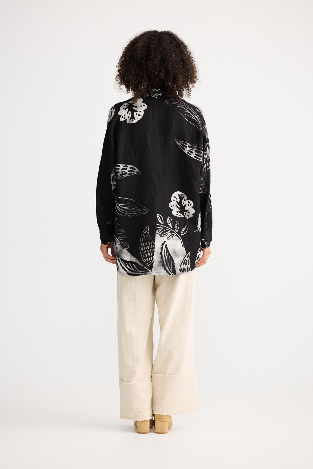 Person wearing a black floral patterned shirt and white pants on a white background