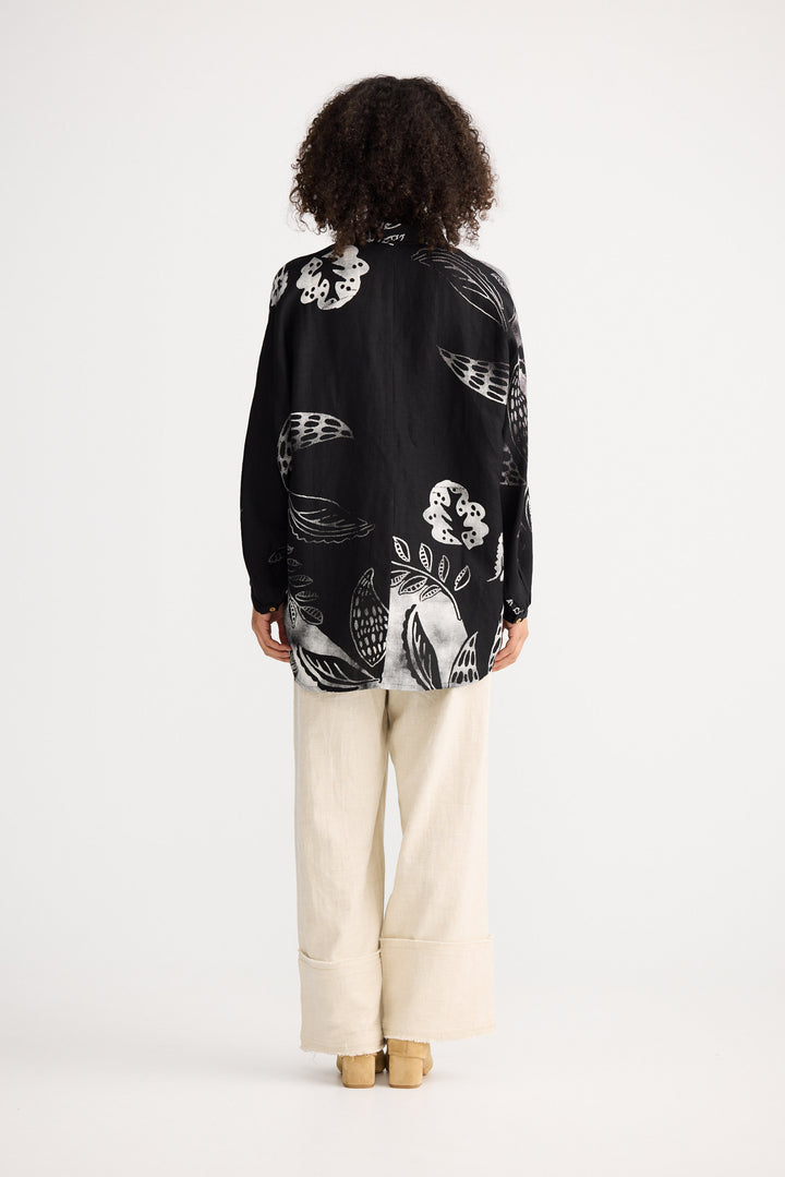 Person wearing a black floral patterned shirt and white pants on a white background
