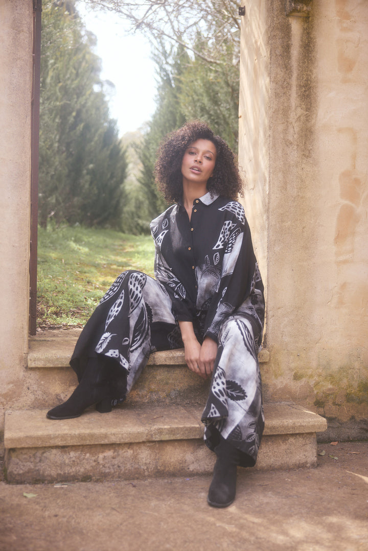Woman in a black and white patterned outfit sitting on stone steps outdoors.