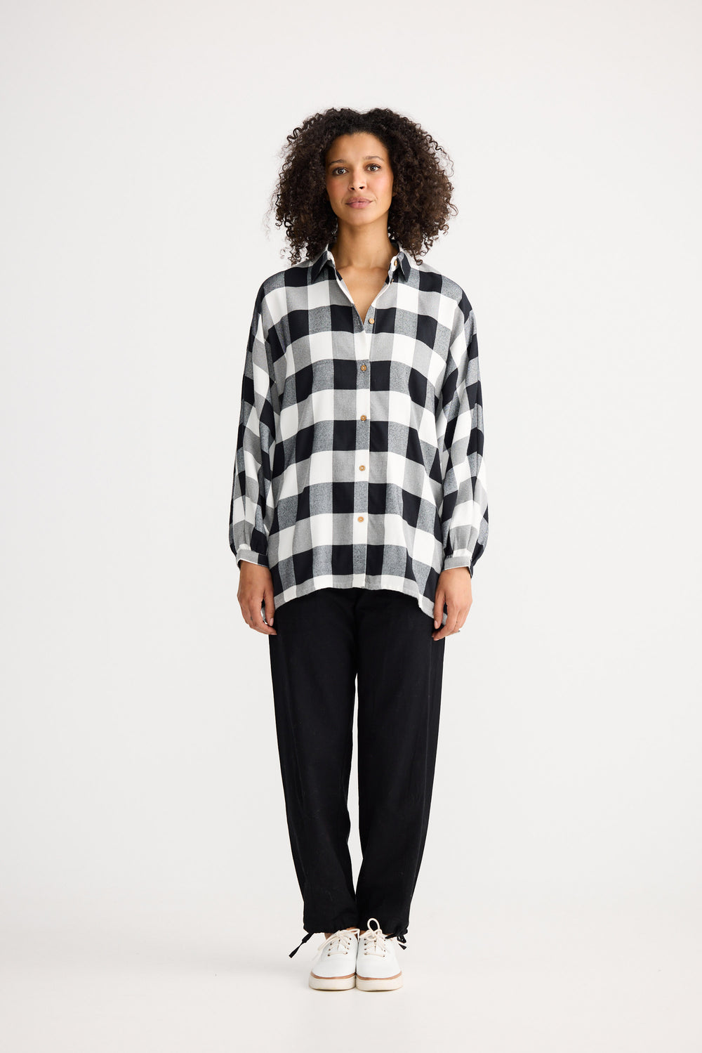 Woman wearing a black and white checkered shirt and black pants on a white background