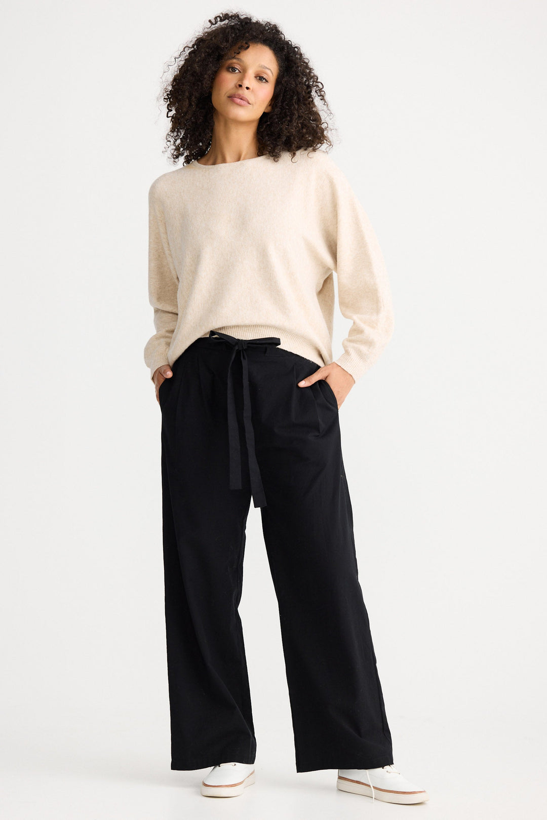 Woman wearing a beige sweater and black pants on a white background