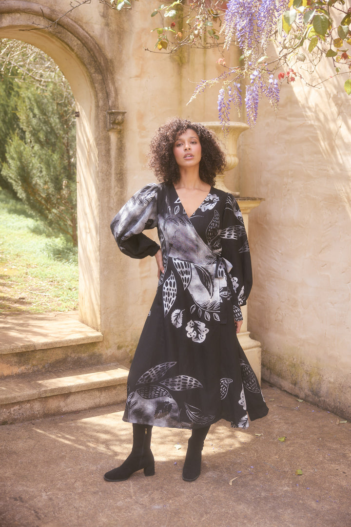 Woman in a black floral dress standing in an outdoor setting with stone architecture and wisteria.