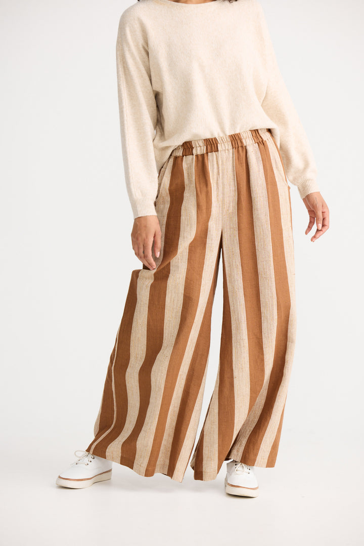 Person wearing a cream sweater and brown and beige striped pants on a white background