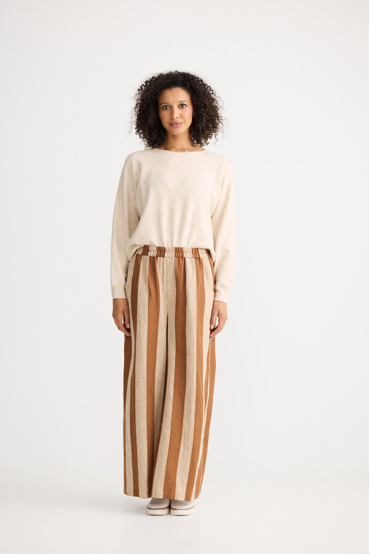 Woman wearing a beige sweater and striped pants on a white background