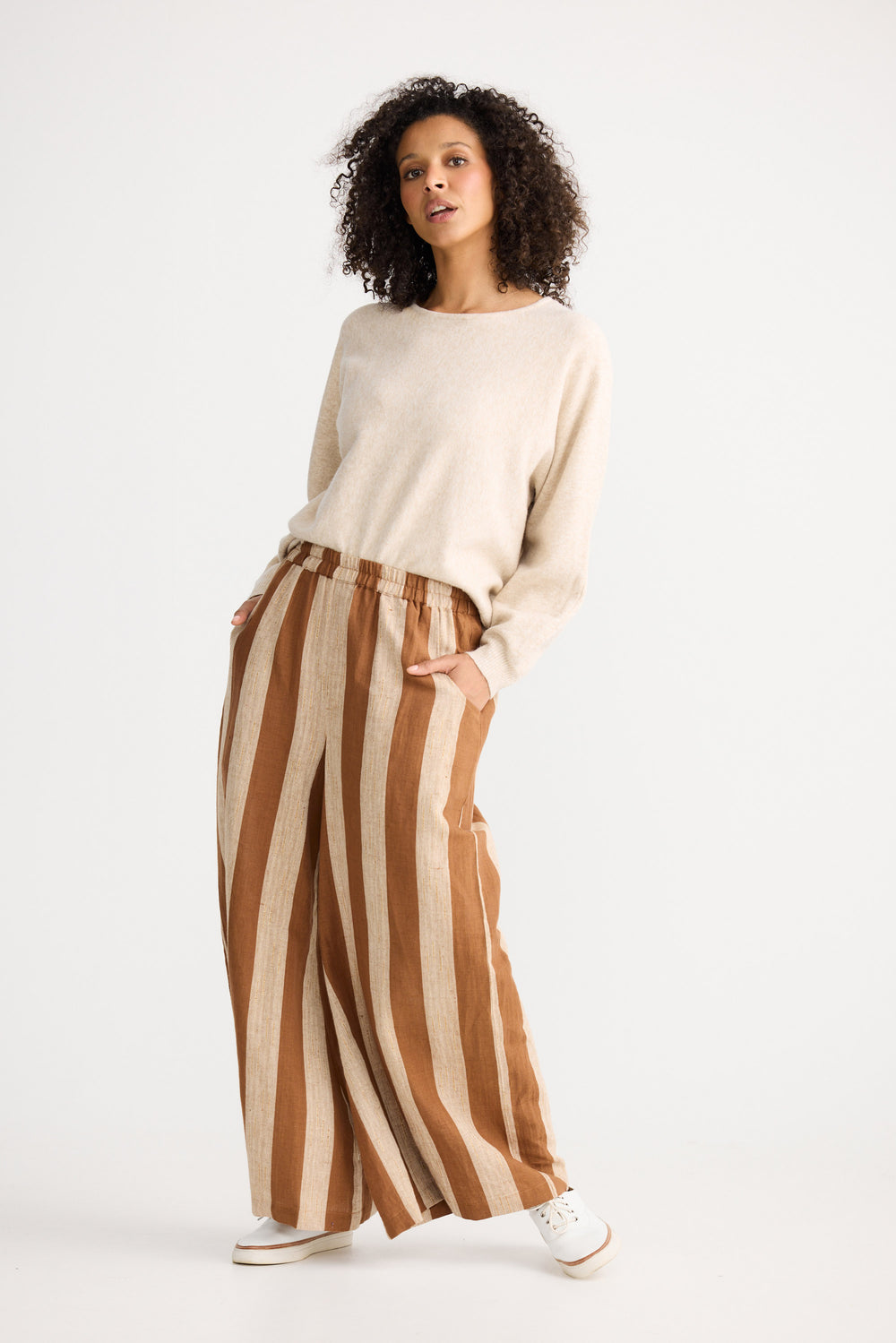Woman wearing a beige sweater and brown striped pants on a white background