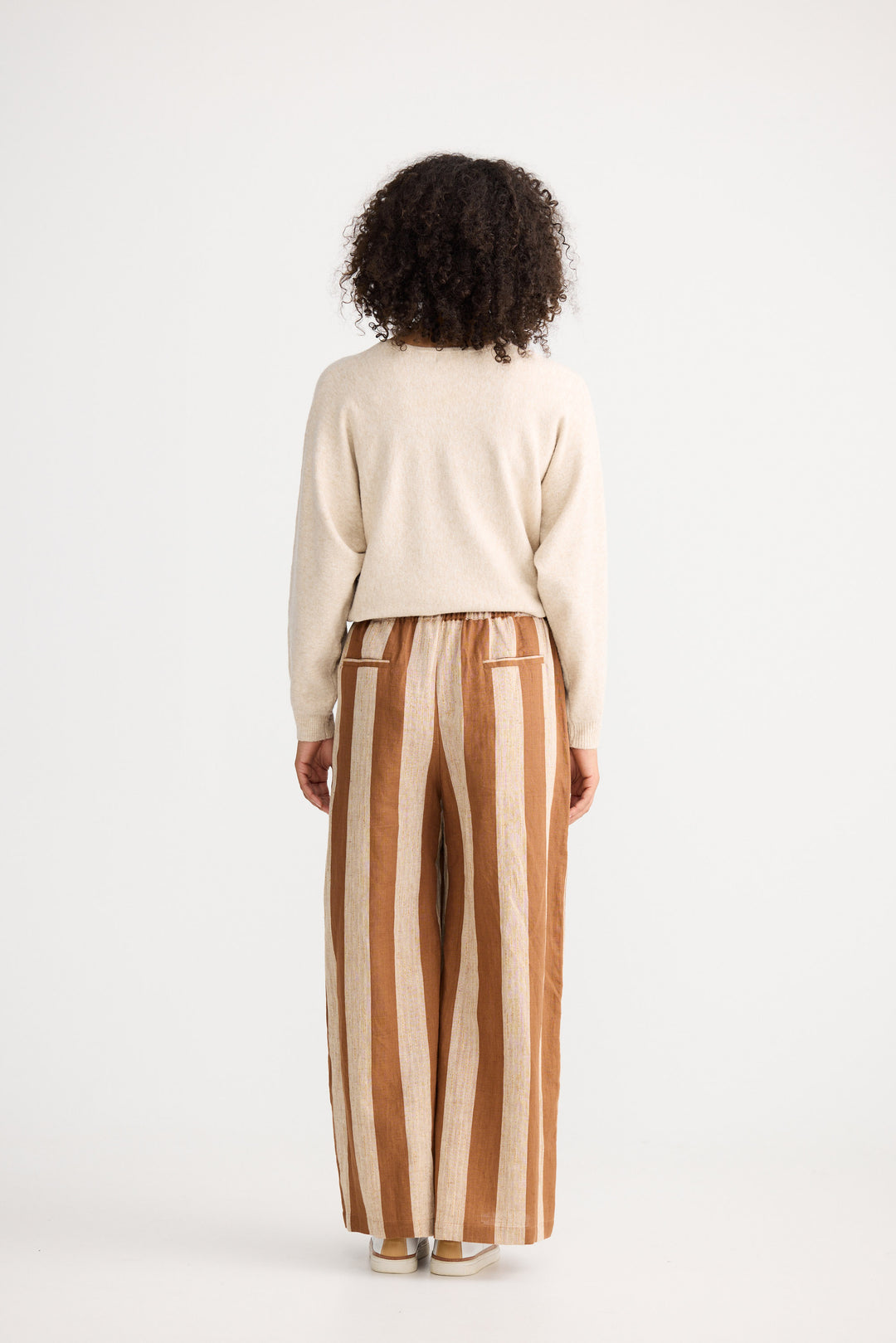 Person wearing a cream sweater and striped pants on a white background