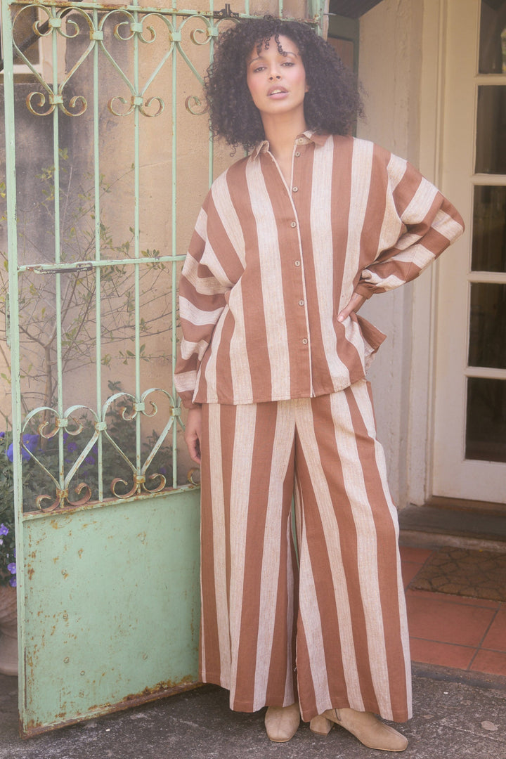 Woman in a striped outfit standing in front of a decorative metal gate and door.
