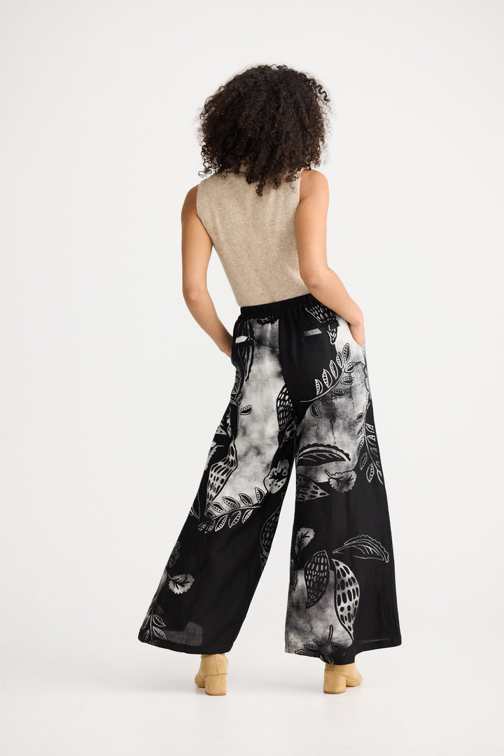 Woman wearing black wide-leg pants with white patterns on a white background