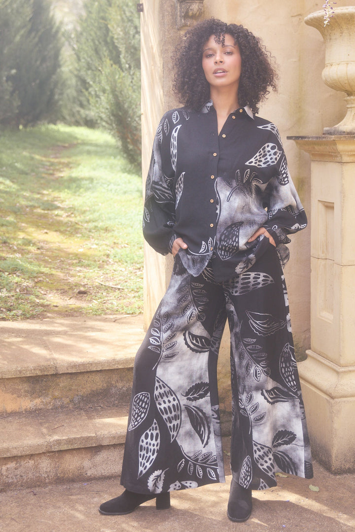 Woman in a patterned outfit standing in a garden with an archway and stone steps.