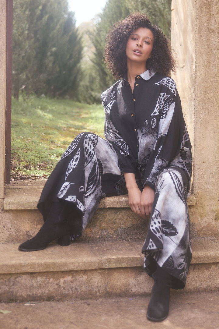 Woman in a black and white patterned outfit sitting on stone steps outdoors.
