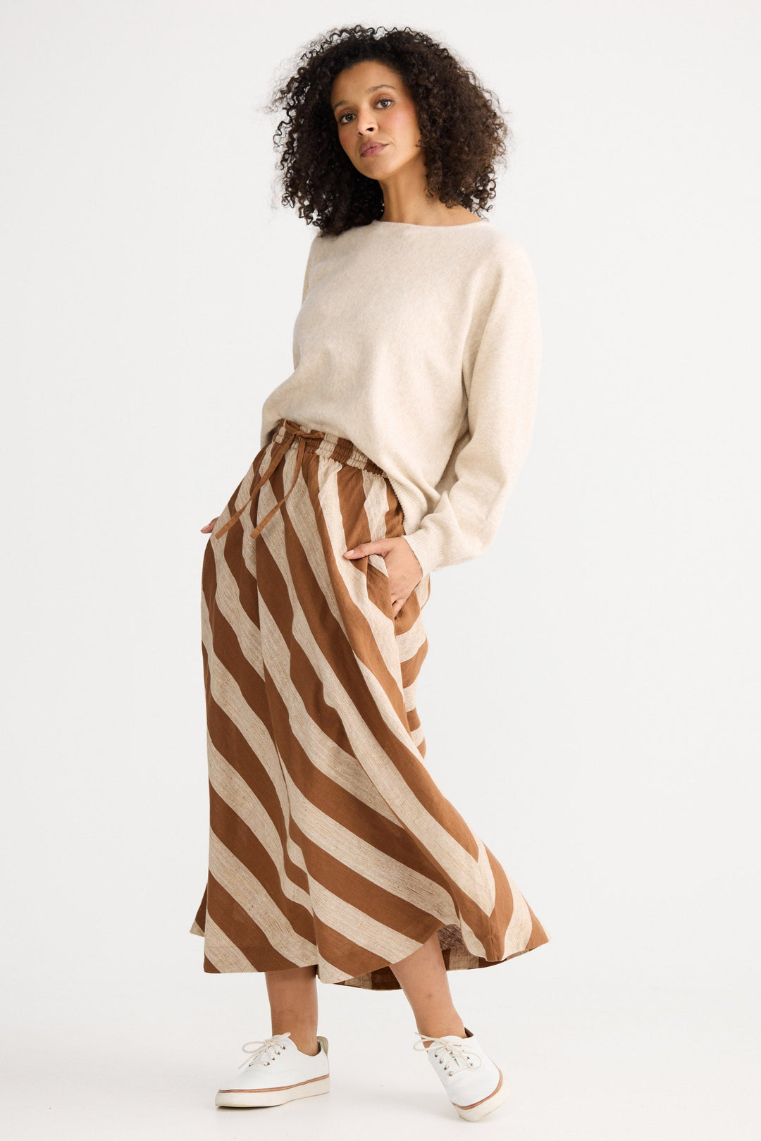 Woman wearing a beige sweater and brown and white striped skirt on a white background