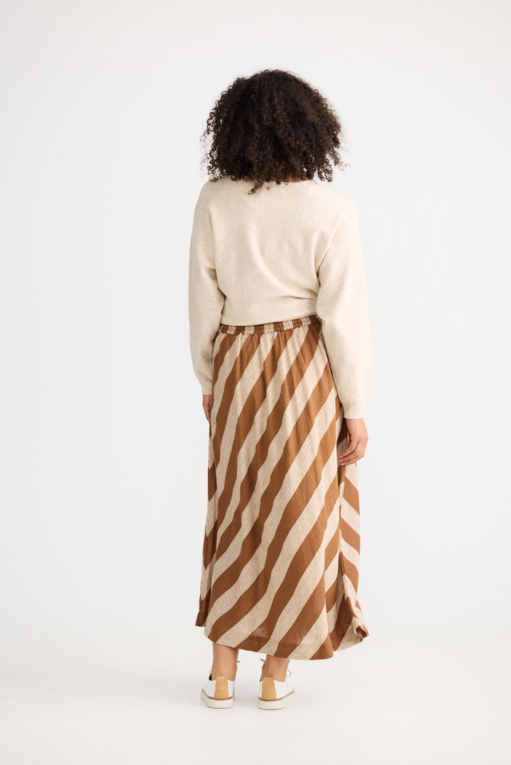 Person wearing a cream sweater and brown and beige striped skirt on a white background
