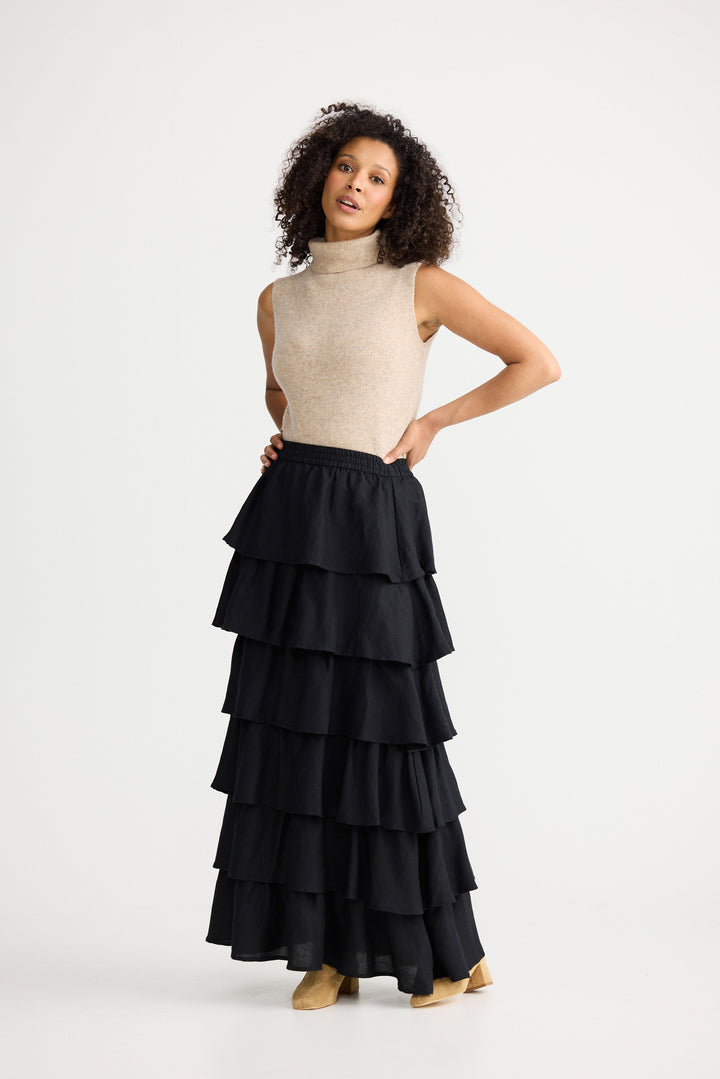 Woman wearing a beige sleeveless top and black tiered skirt on a white background