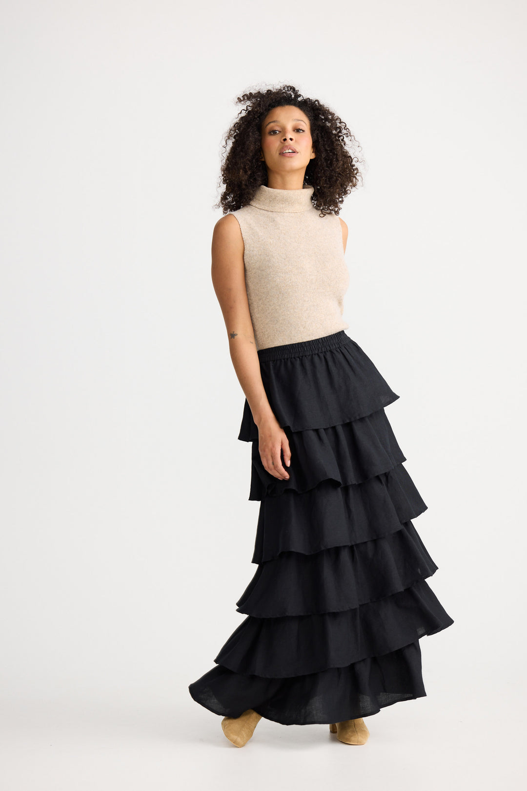 Woman wearing a beige sleeveless sweater and black tiered skirt on a white background